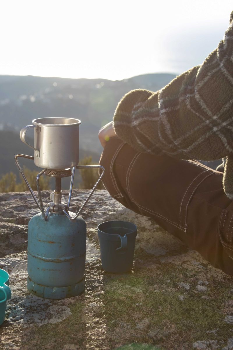person sitting on the side of a mountain with a propane camping stove